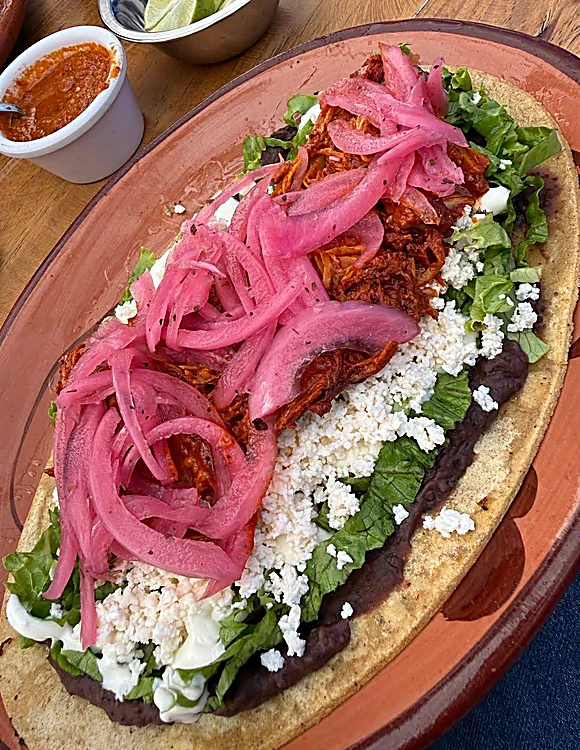Tostada preparada con cochinita pibil, frijoles y cebolla morada