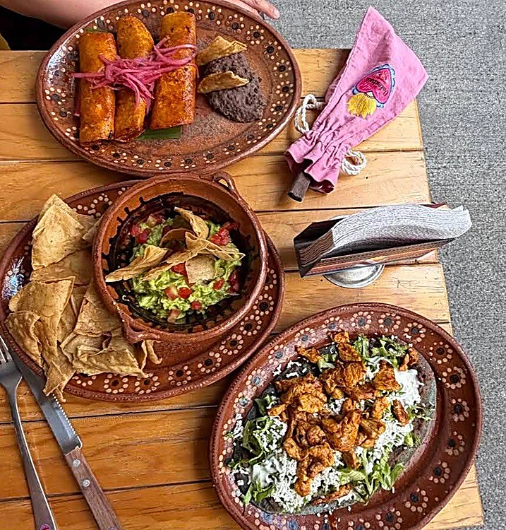 Mesa con flautas, guacamole con totopos y una ensalada con pollo en platos de barro