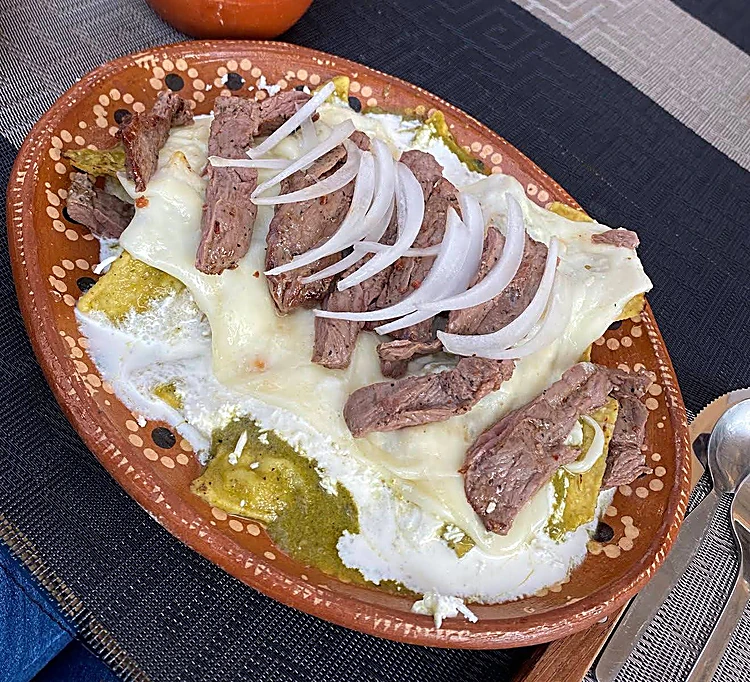 Enchiladas verdes con carne asada, queso gratinado y cebolla en plato de barro